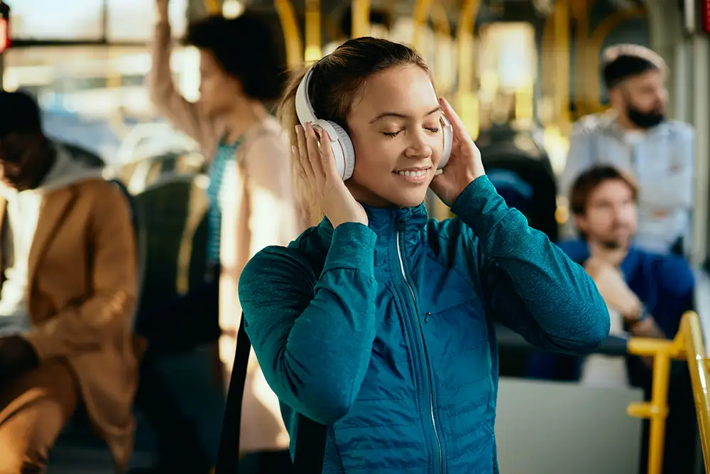 Woman in a busy public place enjoying quiet and focus while wearing noise-cancelling headphones.